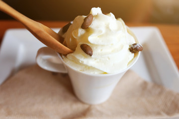 Whipped cream on a cup of fresh hot milk with wood spoon on white dish, Morning time in Cafe at Thailand.