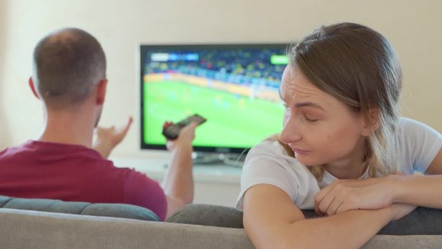 An offended woman sits next to a guy watching a game on TV