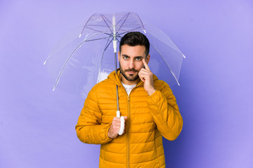 Young handsome man holding an umbrella isolated pointing temple with finger, thinking, focused on a task.