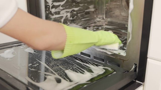 Close up of female hand with gren protective gloves cleaning oven