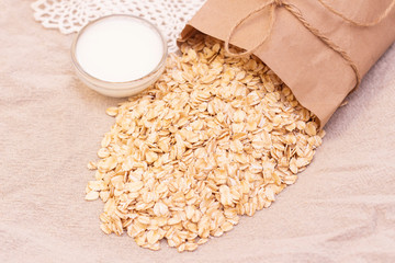 dry natural oat flakes. Oatmeal from an ecological paper bag. Natural linen background with eco bag and oatmeal flakes. A cup of milk