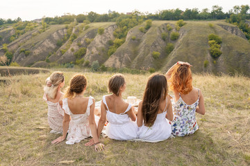 Shoot from back. The company of female friends having fun and enjoy hills landscape.