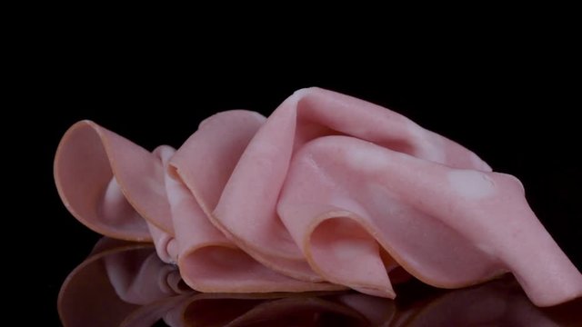 Boiled sausage mortadella rotated on a black background.  Mortadella sausage with a heart, close up.  Gastronomy, meat products. Sausage texture. 