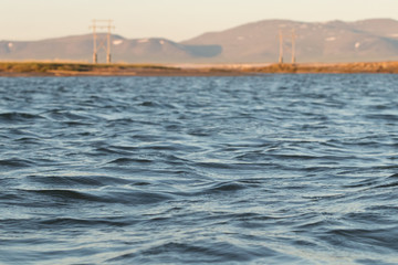 Obraz premium Blue river water in focus, shore with power lines in the background blurred