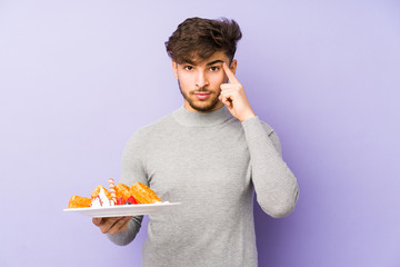 Young arabian man holding a waffle isolated pointing temple with finger, thinking, focused on a task.