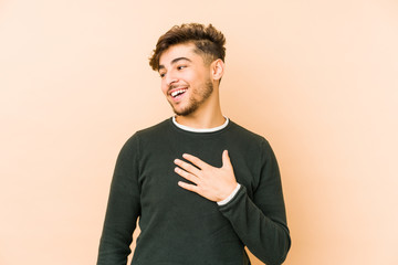 Young arabian man isolated on a beige background laughs out loudly keeping hand on chest.