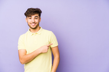 Young arabian man isolated on a purple background smiling and pointing aside, showing something at blank space.