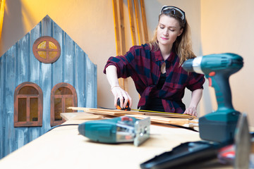 Joinery. A girl in a plaid shirt makes a wooden house for the Playground. Marking of bars. Carpentry tool. The work of the joiner. Working with wood is a hobby.