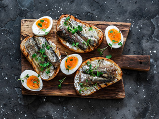 Delicious appetizer, tapas - soft boiled eggs and canned sardines sandwiches on a cutting board on...