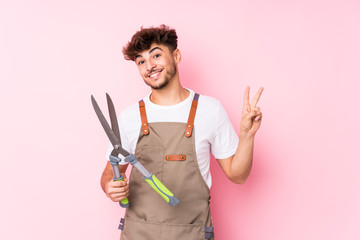 Young arab gardener man isolated joyful and carefree showing a peace symbol with fingers.