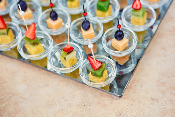 Assorted canapes of fruit and cheese on a glass platter on the background of glasses and champagne. Catering