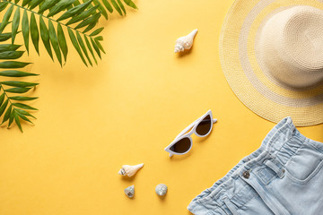 Fototapeta na wymiar straw hat, sunglasses, blue denim shorts and palm leaves on a yellow background. concept summer holiday background. horizontal image. copy space