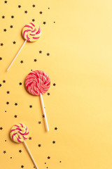 festive background with lollipops and sparkles on a yellow background. Birthday or party decor. vertical image, banner.