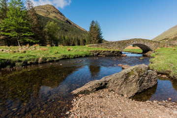 Fototapeta na wymiar Ancient stone bridge crossing a tranquil river in Scotland