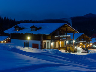 Ski resort Gornaya Salanga at night. Blue twilight is falling, a yellow cozy warm light has lit up in the houses. Winter in Siberia