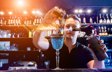 The bartender makes a cocktail with a fire show at the bar. Bartender at work.