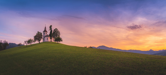 Breathtaking panorama with the view of beautiful colorful summer sunset in Slovenian Alp mountains with St Tomaz church. Travel destination Slovenia