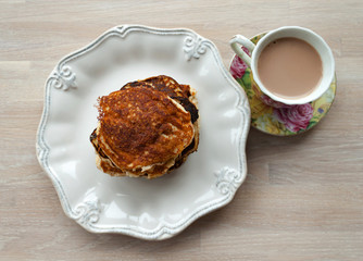 Low Carb Keto Diet Pancakes from almond coconut flour stack on white plate and cup of cocoa on wooden table background close up view. Selective focus. Copy space. Ketogenic concept