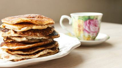 Low Carb Keto Diet Pancakes from almond coconut flour stack on white plate and cup of cocoa on wooden table background close up view. Selective focus. Copy space. Ketogenic concept