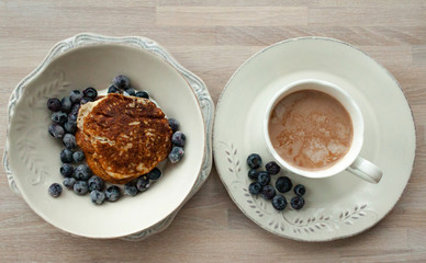 Low Carb Keto Diet Pancakes from almond coconut flour with blueberries, cream on white plate and cocoa cup on wooden table background close up view. Selective focus. Copy space. Ketogenic concept