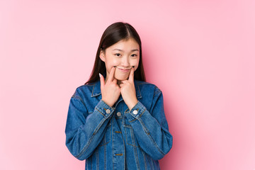 Young chinese woman posing in a pink background isolated doubting between two options.