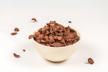 Chocolate corn flakes falling to the white bowl isolated on white. Motion.