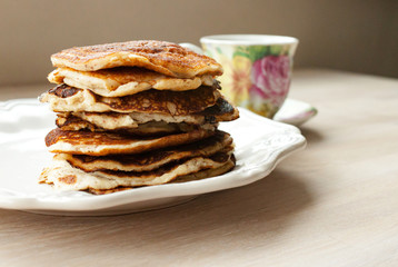 Low Carb Keto Diet Pancakes from almond coconut flour stack on white plate and cup of cocoa on wooden table background close up view. Selective focus. Copy space. Ketogenic concept