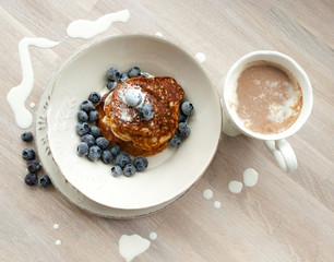 Low Carb Keto Diet Pancakes from almond coconut flour with blueberries, cream on white plate and cocoa cup on wooden table background close up view. Selective focus. Copy space. Ketogenic concept