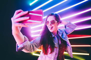Portrait of modern young woman making selfie at the neon light.