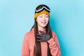 Young chinese woman wearing ski clothes isolated laughs out loudly keeping hand on chest.
