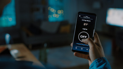 Close Up Shot of a Smartphone with Active Smart Home Application. Person is Tapping the Screen To Turn Lights On/Off in the Room. It's Cozy Evening in the Apartment. 