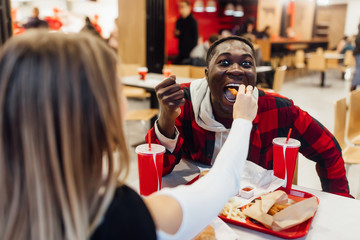 Obraz premium Couple in love feeding each other together. Man in checkered shirt, woman in sweater. Fast food concept.