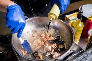 Chef cooking pasta with mussels in pan. Italian style cuisine. Restaurant.