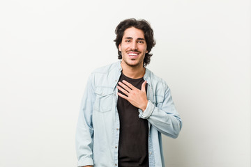 Young handsome man against a white background laughs out loudly keeping hand on chest.