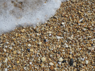 Small smooth pebbles and worn glass line the beach at low tide in the coastal community of Sea Girt New Jersey on the Atlantic Coast as small foamy waves wash over them