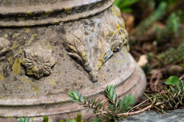 Inverse broken ceramic plant pot with ornamental sculptures on ground of flowerbed.