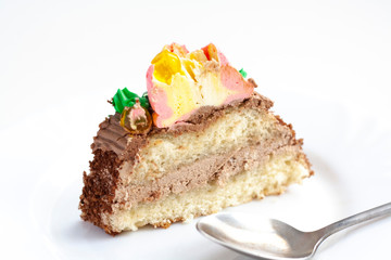 A piece of biscuit cake with colored cream on a white plate, a spoon