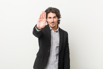 Young business man against a white background standing with outstretched hand showing stop sign,...
