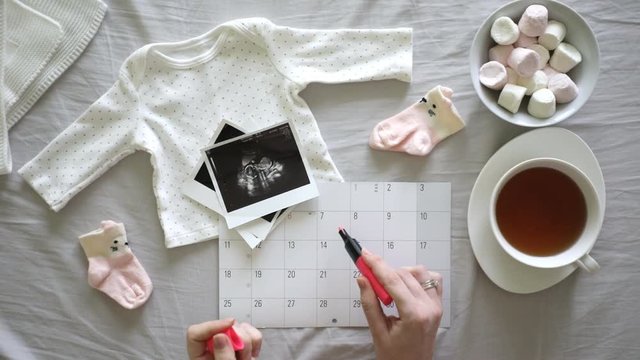Top vew of expecting pregnant woman notes the date of birth on the calendar at home, pregnancy and birth concept