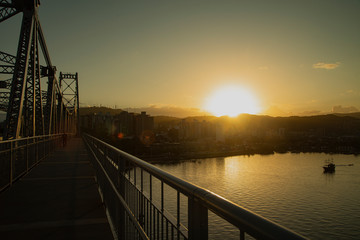 Obraz premium View of city's downtown through walkway of Hercílio Luz bridge at Sunrise hour, landmark of Florianópolis city, Brazil. 