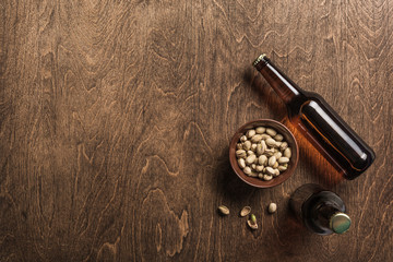 Two dark beer bottles and a plate of pistachios on a wooden background.