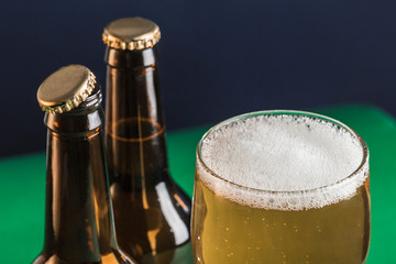 Two dark fogged beer bottles and a glass of beer and foam on a green and blue background.