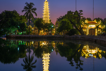 Hanoi buddhist pagoda (Tran Quoc Pagoda) on West Lake at Hanoi, colorful sunset, illuminated temple, water reflection. Vietnam travel.