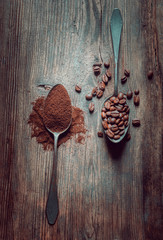 Top view of different varieties of coffee: ground and in beans, lying in two same wooden spoons on black mat background.