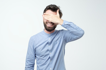 Young happy hispanic man screaming and covering eyes with hands