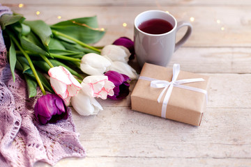 Spring flowers. Tulips, gift box and white cup of tea at wooden background. White, pink, lilac and purple bouquet. Morning surprise. Still life.