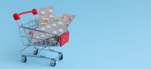 The trolley for the supermaquet is loaded with medicines, on a blue background, the concept of medicine, space for text