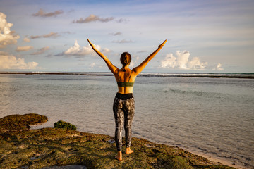 Excited young woman raising arms at the beach in front of the ocean. View from back. Freedom and energy. Bali, Indonesia.