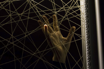 The girl's hand drags its fingers to the net of threads that create a geometric pattern intersecting each other