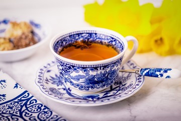 A cup of tea with anise star. White and blue dishes and yellow daffodils